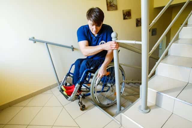 person Sitting on a Wheelchair assisting himself on the Stairs
