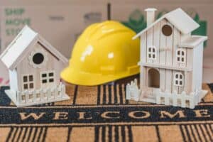 Miniature wooden houses on a welcome mat with a yellow hard hat