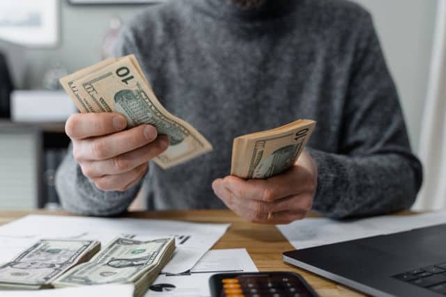 person counting cash with a calculator and paperwork